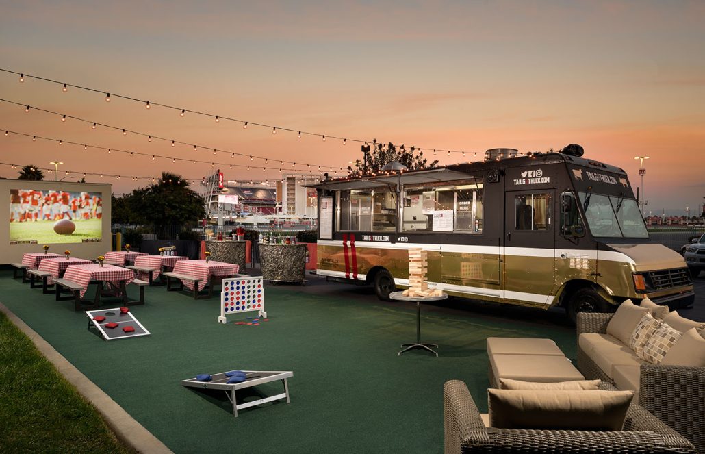 Outdoor tailgate venue at Hilton Santa Clara with picnic tables, string lights, and a food truck near Levi’s Stadium